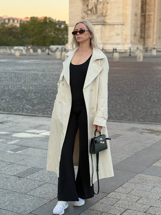 The Amélie trench coat in stone, full-length front view beside a stone arch
